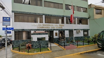 Fachada de la Comisaría San Miguel de la Policía Nacional del Perú, con una bandera peruana, señales de tráfico y motocicletas estacionadas