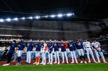 Vista lateral de once jugadores de béisbol de los Houston Astros de pie en el campo verde de un estadio iluminado, la mayoría con chaquetas azules