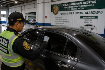 Un agente mide la opacidad del vidrio de un automóvil oscuro con un medidor digital junto a un cartel sobre lunas polarizadas