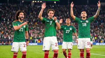 Cuatro jugadores de fútbol mexicanos, en camisetas verdes con patrones geométricos y shorts blancos, celebran en un estadio con público.