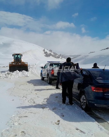 Una máquina quitanieves retira la nieve sobre un camino junto a un patrullero de la Policía de Neuquén y un automóvil oscuro con personas cerca