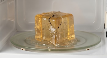 Cubo de gel agrietado y derretido en parte sobre el plato giratorio dentro de un microondas