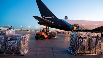 Avión de carga Amazon Prime en la pista de un aeropuerto, siendo cargado por un montacargas naranja con palés de suministros de emergencia embalados