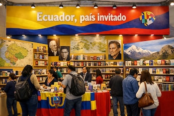 Pabellón de Ecuador con estanterías llenas de libros, mapas en la pared, retratos de autores y una pancarta que dice 'Ecuador, país invitado'. Personas circulan.