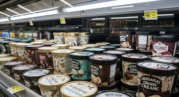Vista de cerca de un congelador de supermercado lleno de múltiples envases cilíndricos de helado orgánico artesanal, con tapas beige y etiquetas coloridas.