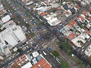 Do alto, uma grande multidão se aglomerava em uma rua e em uma área verde arborizada, cercada por estruturas de aço.