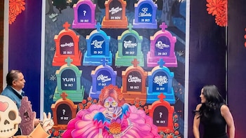 Póster de evento. Calavera femenina con vestido rosa. Varias lápidas con nombres de artistas y fechas. Hombre y mujer observando. Recorte de esqueleto