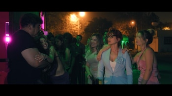 Un grupo de amigos sonríe y abraza en una discoteca con iluminación verde, rosada y naranja, reflejando un ambiente de fiesta