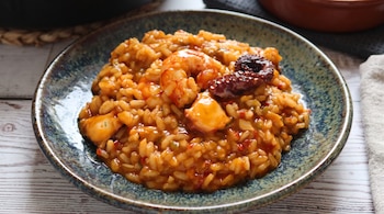 Arroz meloso con trozos de pulpo y un gambón servido en un plato hondo de cerámica sobre una superficie de madera.