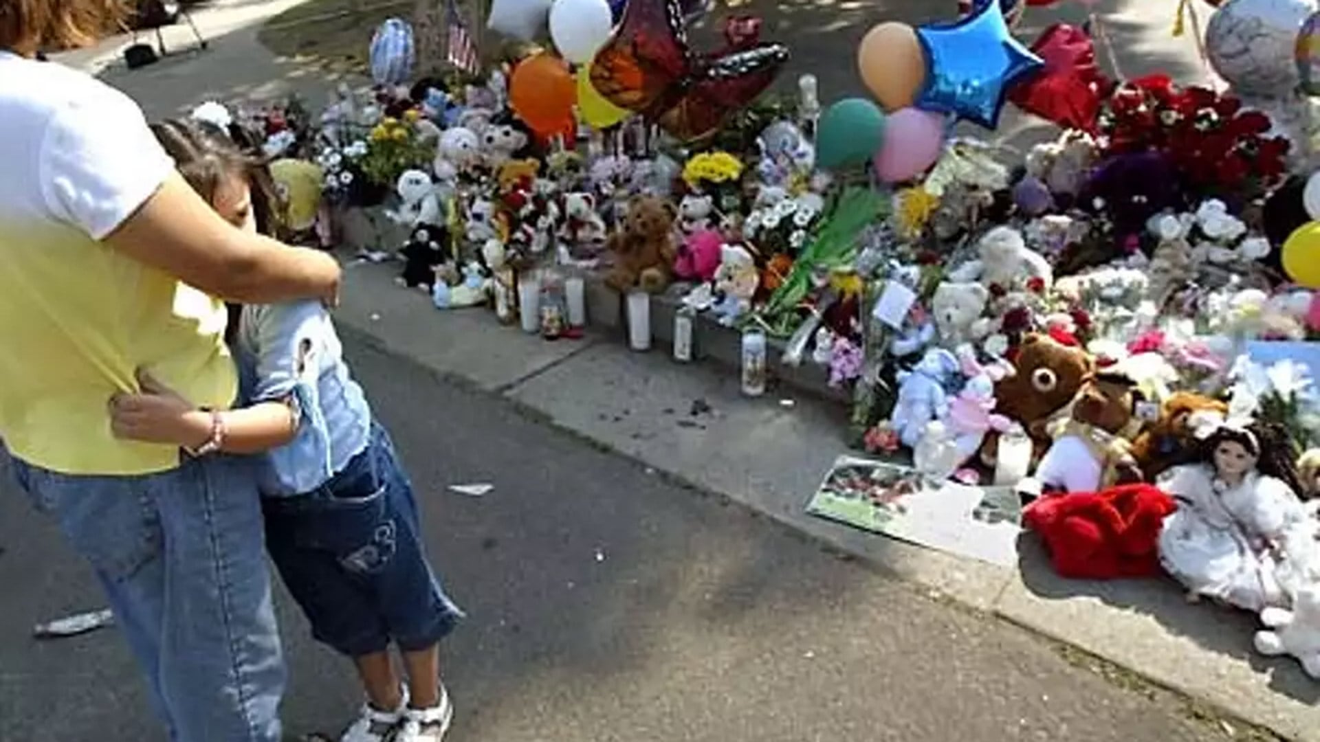 Liliana Torres, de 6 años, abraza a su madre, Benita, mientras rinden homenaje en un memorial para las víctimas situado en la vereda frente a la casa de Marcus Wesson en Fresno, California, el lunes 15 de marzo de 2004 (AP Photo/Jeff Chiu)