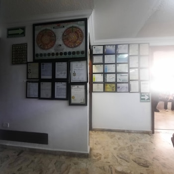 Interior de una clínica con paredes blancas, diplomas y certificados enmarcados, un gran póster de iridología y un letrero de ruta de evacuación