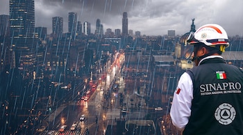 Persona de espaldas con casco blanco y chaleco oscuro de SINAPROC, observando una ciudad con rascacielos, tráfico vehicular y lluvia intensa.
