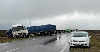 Un camión dañado en la banquina de una ruta mojada, un automóvil blanco detenido a la derecha y personas sobre el asfalto