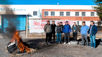 Grupo de hombres protestando frente a la fábrica Soltex con una pancarta, neumáticos quemándose con humo negro y un edificio blanco al fondo