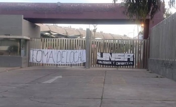 La entrada principal de la Universidad Nacional de San Agustín, con rejas metálicas cerradas y dos pancartas de protesta: "TOMA DE LOCAL" y "UNSA VALIENTE Y COMBATIVA"