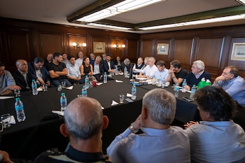 Un grupo de personas sentadas alrededor de una mesa con mantel negro durante una reunión en una sala con paneles de madera