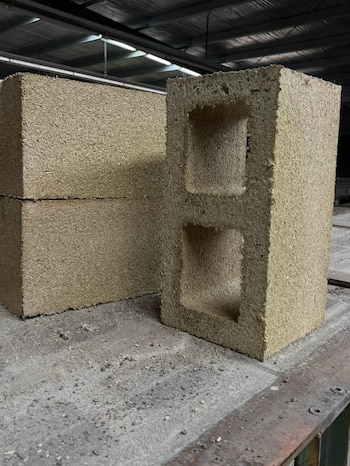 Primer plano de dos bloques de construcción de color beige con textura fibrosa. Uno de ellos, vertical, muestra dos orificios rectangulares. Otro bloque se apila detrás