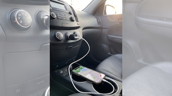 Interior de un automóvil con tablero y asiento de pasajero. Un teléfono móvil con mapa se carga con cable USB conectado a un adaptador en el encendedor.