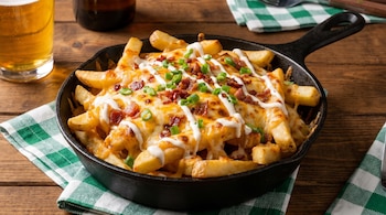 Papas fritas en una sartén de hierro fundido, cubiertas con queso cheddar fundido, tocino crujiente, crema agria y cebollino picado, sobre una mesa de madera.