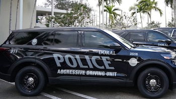 Vehículo SUV policial negro. En el lateral se lee "Police", "Doral", "Aggressive Driving Unit", "911" y "2516". Hay palmeras al fondo