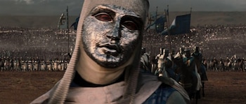 Primer plano del Rey Balduino IV con una máscara facial plateada ornamentada y cota de malla, frente a un vasto ejército medieval en formación