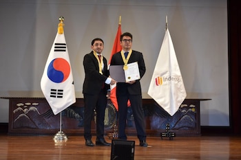 Tres personas posan en un escenario frente a las banderas de Corea del Sur y Perú mientras la del centro sostiene una medalla y un diploma