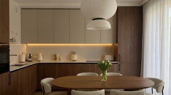 Una cocina pequeña con encimeras blancas, gabinetes de madera y beige, y electrodomésticos Smeg. En el centro, una mesa de comedor de madera con sillas blancas y tulipanes.