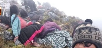 Varias personas, algunas con ropa tradicional, yacen en una ladera rocosa y herbosa cubierta de niebla. Se observa un gorro con la palabra "CUSCO"