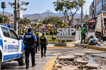 Agentes de serenazgo y policía caminan junto a un vehículo municipal, un letrero de San Martín de Porres y un trabajador de limpieza