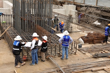 Trabajadores con cascos y chalecos de seguridad revisan un plano junto a una estructura de varillas de acero en una excavación