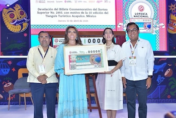 Cuatro personas, dos hombres y dos mujeres, posan sonrientes en un escenario, sosteniendo un billete de lotería conmemorativo grande y enmarcado