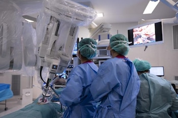 Personal médico con batas quirúrgicas opera a un paciente mediante un brazo robótico en un quirófano equipado con pantallas