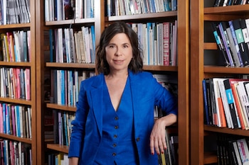 La periodista María O'Donnell sonríe, vistiendo un traje azul de blazer y chaleco, de pie frente a una estantería de madera llena de libros