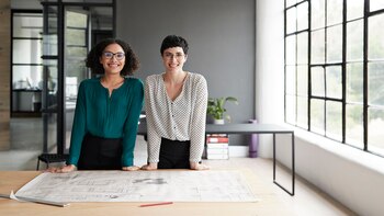 Portrait of smiling businesswomen standing by table in office