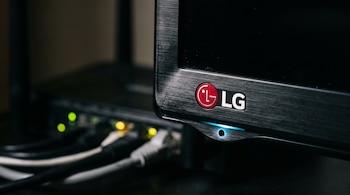 Esquina de un televisor LG con un micrófono integrado e iluminado delante de un enrutador de red con cables.