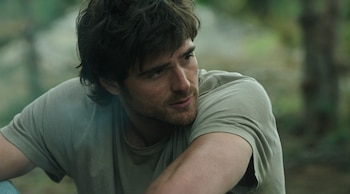 Primer plano de un hombre joven con cabello oscuro y barba, mirando hacia la izquierda del encuadre. Viste una camiseta verde claro. Fondo desenfocado