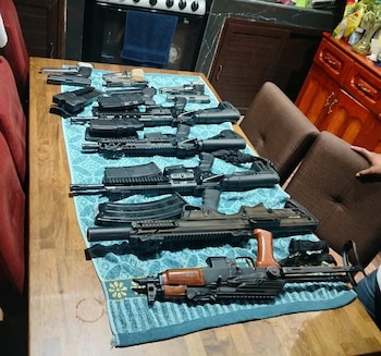 Varias pistolas, fusiles y cargadores de munición están colocados sobre una toalla azul encima de una mesa de madera