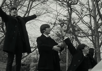 Fotografía en blanco y negro de tres hombres jóvenes, Ringo Starr, John Lennon y George Harrison, de The Beatles, con brazos en alto en un parque con árboles desnudos
