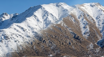 Imagen comparativa de una montaña: el lado izquierdo cubierto de nieve blanca brillante, el lado derecho con vegetación marrón y rocas expuestas, bajo un cielo azul claro.