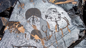 Grabados sobre una roca oscura con diseños de figuras estilizadas y motivos circulares.
