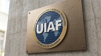 Vista diagonal de una placa metálica rectangular con el logo circular de la UIAF, con un mapa mundi y números binarios, sobre una pared de concreto.