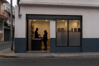 Fachada de un local comercial iluminado en una calle urbana con las siluetas de dos personas conversando en el interior.