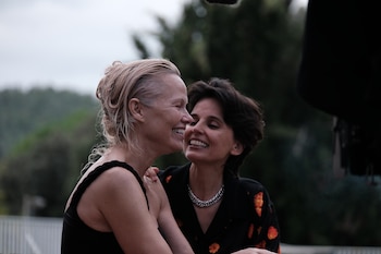 Dos mujeres, una rubia de cabello mojado con vestido negro y otra morena de cabello corto con camisa oscura estampada, se ríen con sus rostros muy cerca