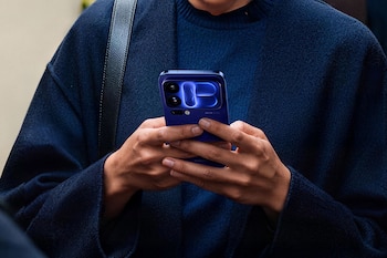 Manos de una persona sujetando un teléfono móvil azul con cámaras Leica y una pantalla luminosa posterior