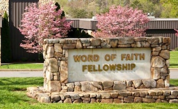 Un letrero de piedra con las palabras Word of Faith Fellowship frente a un edificio con árboles de flores rosadas