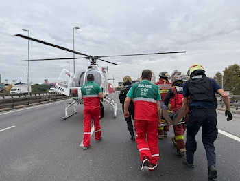 Equipo de S.A.M.E. y Bomberos en una autopista, llevando a una persona en camilla hacia un helicóptero blanco con rotor en movimiento bajo un cielo nublado