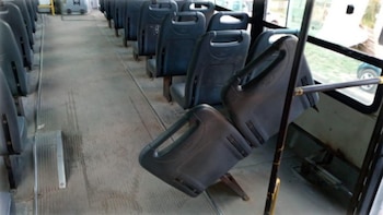 Interior de un vagón de tren con asientos grises alineados a ambos lados de un pasillo central. Un asiento está inclinado hacia arriba y se ve una ventana