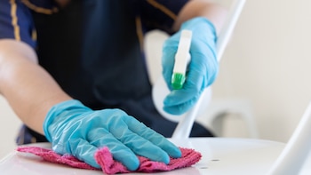 Unas manos con guantes, un paño y un pulverizador limpiando una superficie.