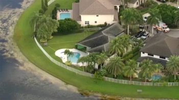 Vista aérea de casas residenciales con piscinas, jardines, un lago y vehículos de emergencia estacionados en la calle