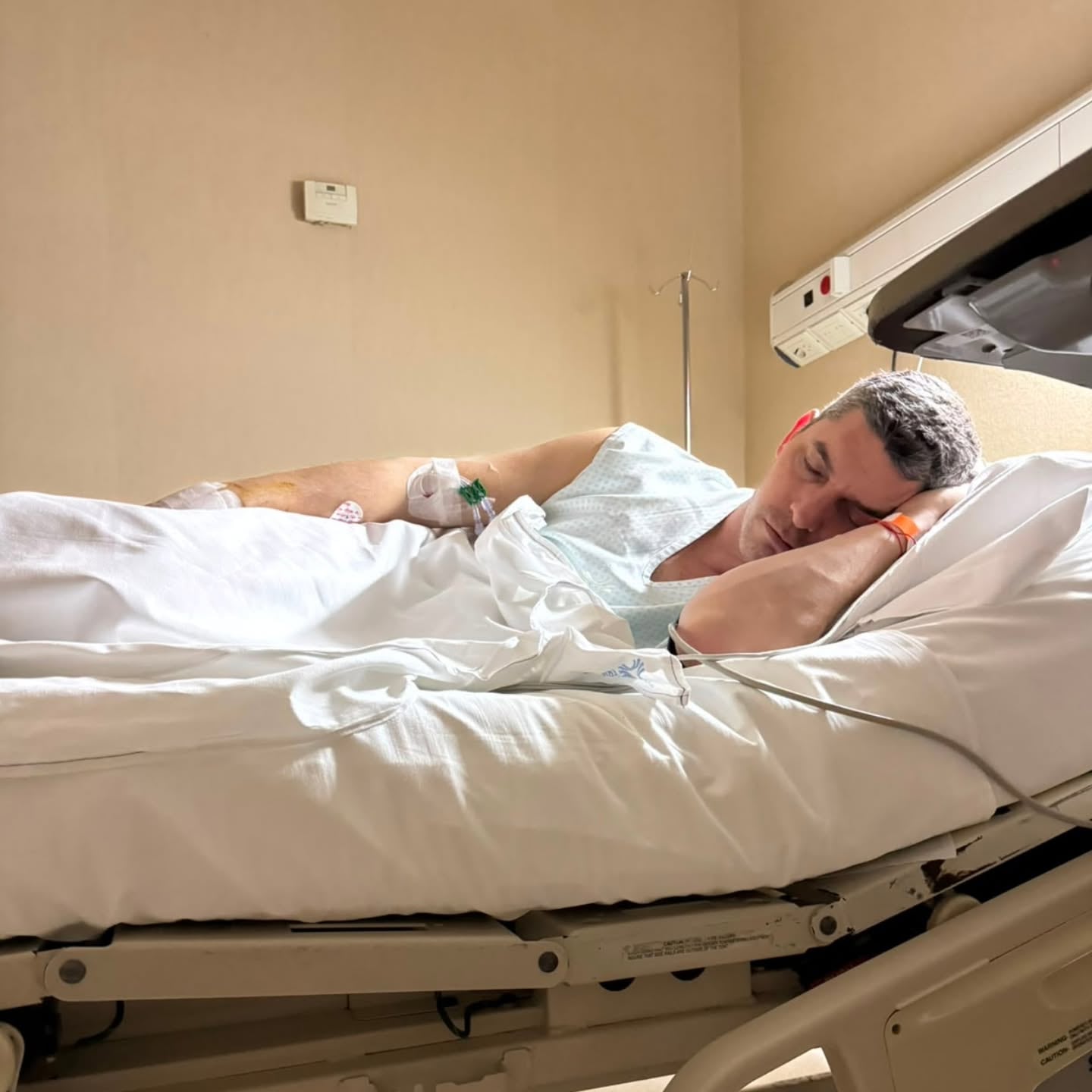 El periodista Santiago Martella descansa en una cama de hospital con una vía intravenosa en el brazo durante su tratamiento médico.